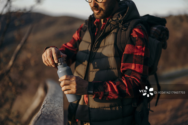 自信的年轻男人在山上行走，喝水并背着背包，享受自由和运动图片素材