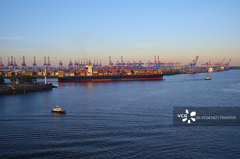 德国汉堡易北河日出时分的港口景色，有集装箱船、起重机和平静的水面图片素材