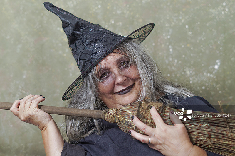 手持扫帚微笑的戴黑帽白发老巫婆图片素材