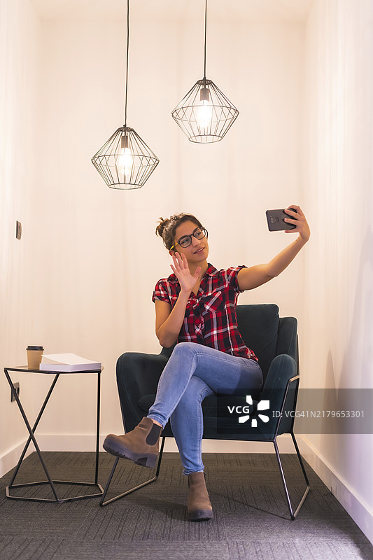 女人在家中舒适的房间里用手机进行视频通话，并向镜头挥手图片素材