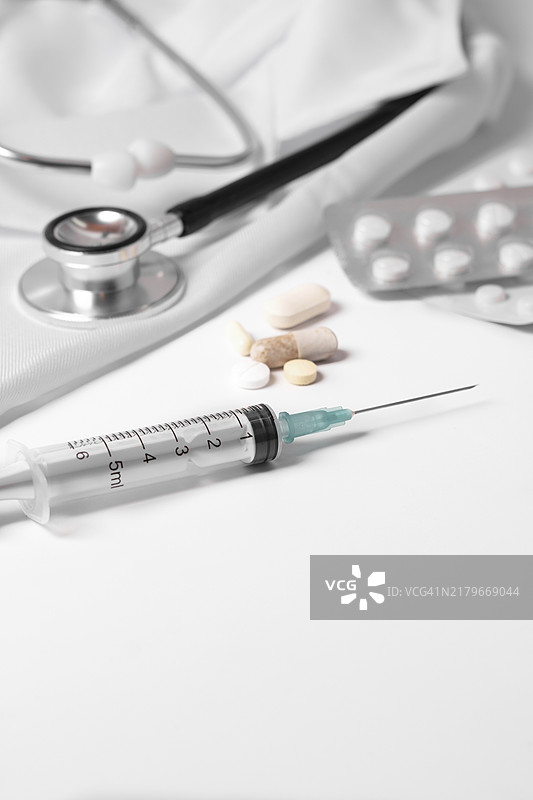 听诊器、药片、注射器在医生白大褂上。白色背景。图片素材