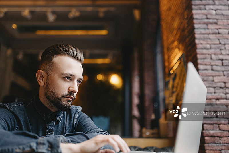 在共享空间用笔记本电脑热情工作的、专注的年轻有为的自由职业者，身穿牛仔衬衫图片素材