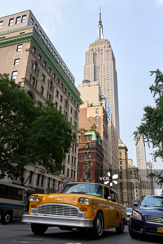 黄色出租车在街道上行驶，背景是帝国大厦。图片素材