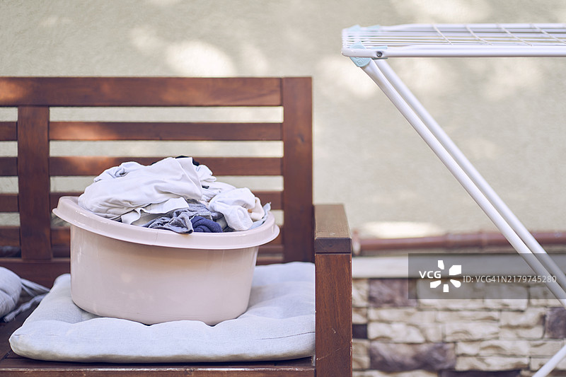 一个放在烘干机旁的长椅上的洗衣盆，体现了洗衣服的概念。图片素材