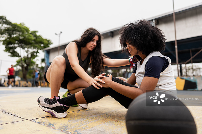 篮球运动员女性在运动场上帮助受伤的朋友图片素材