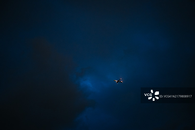 飞机翱翔在深邃的蓝色夜空中，灯光隐约照亮了它的路径图片素材
