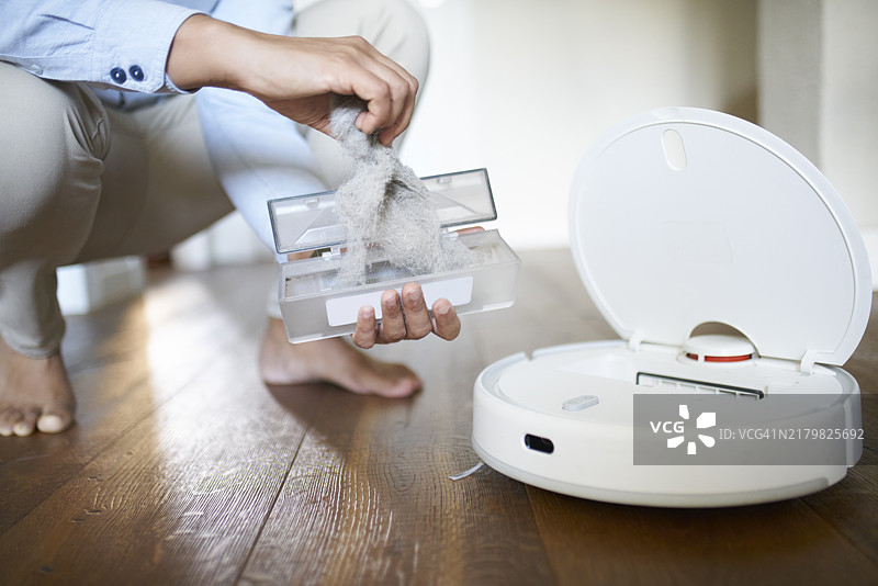 男人清理扫地机器人集尘盒中的灰尘图片素材