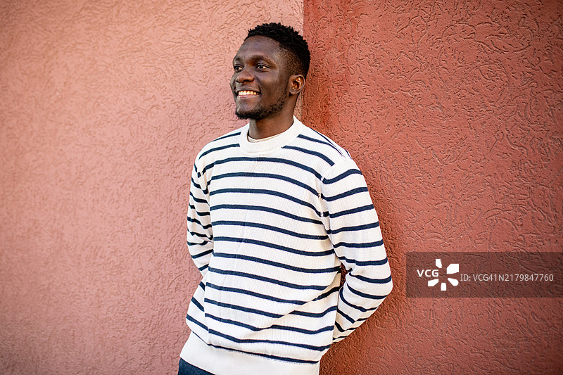 年轻帅气的黑人男子站在红色墙壁前微笑。图片素材