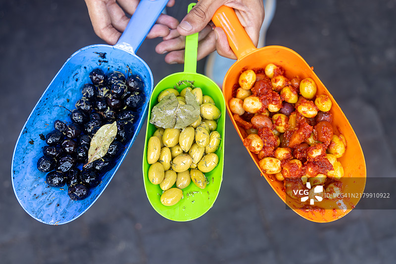 在摩洛哥北非马拉喀什的市集上，手持不同种类橄榄样品进行销售的人图片素材