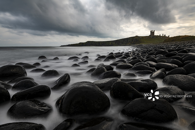 大不列颠诺森伯兰郡克拉斯特，邓斯坦堡城堡后海浪中的黑色圆形岩石和乌云图片素材