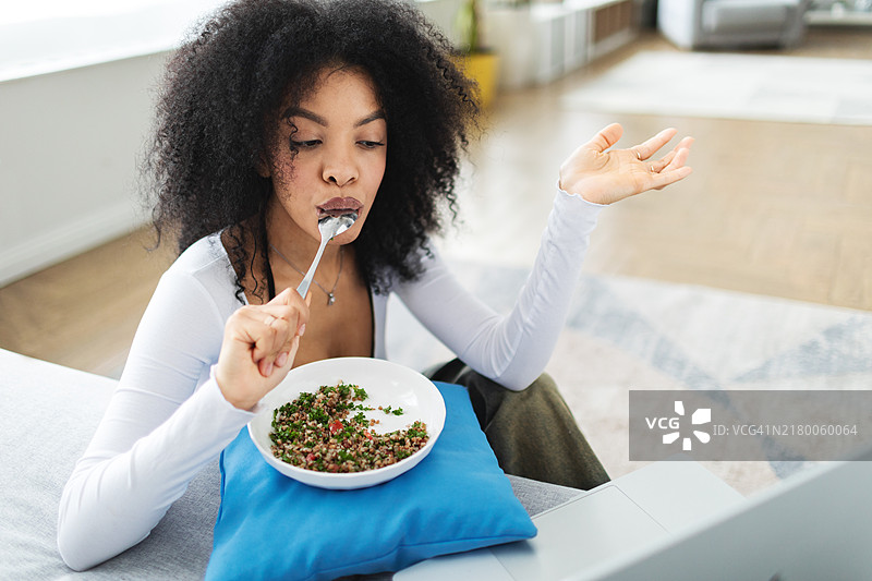 年轻女子使用笔记本电脑吃东西和进行视频通话图片素材