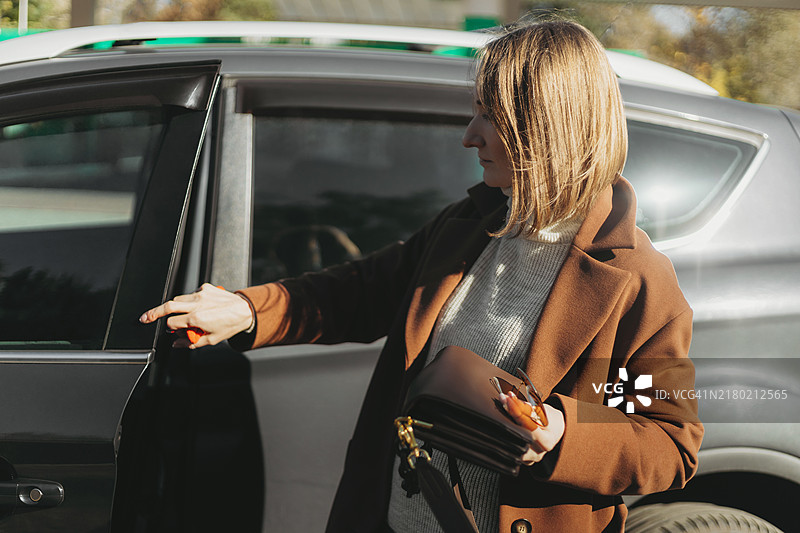 年轻女子穿着外套，正在关一辆SUV的车门。图片素材