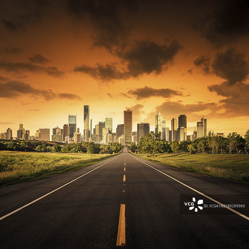 一条通往大型城市天际线的长路，笼罩在阴沉的橙色天空下图片素材