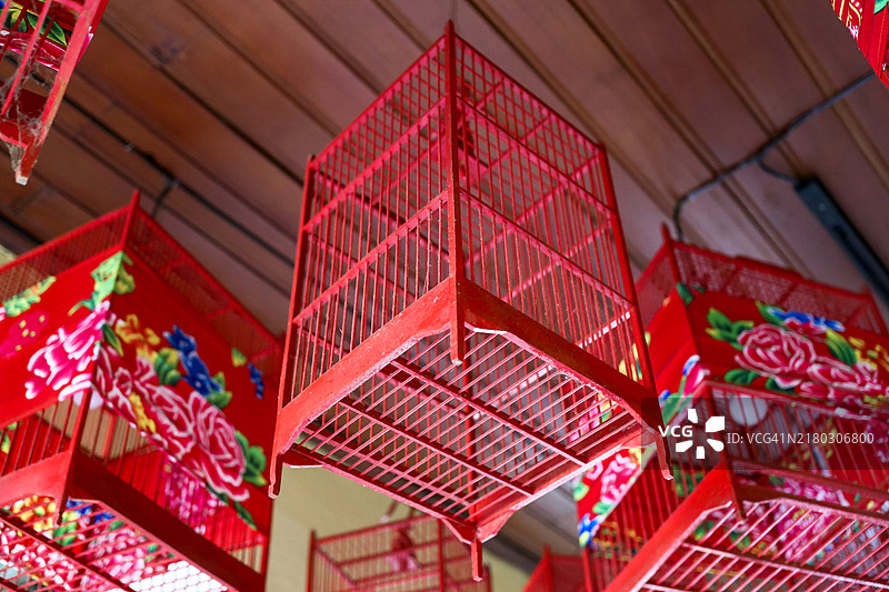 覆盖着孔雀花纹布的红色空鸟笼图片素材