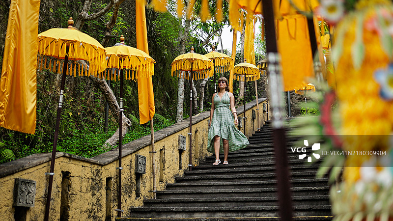 女子在巴厘岛GWK文化公园的寺庙台阶上撑着黄伞行走图片素材