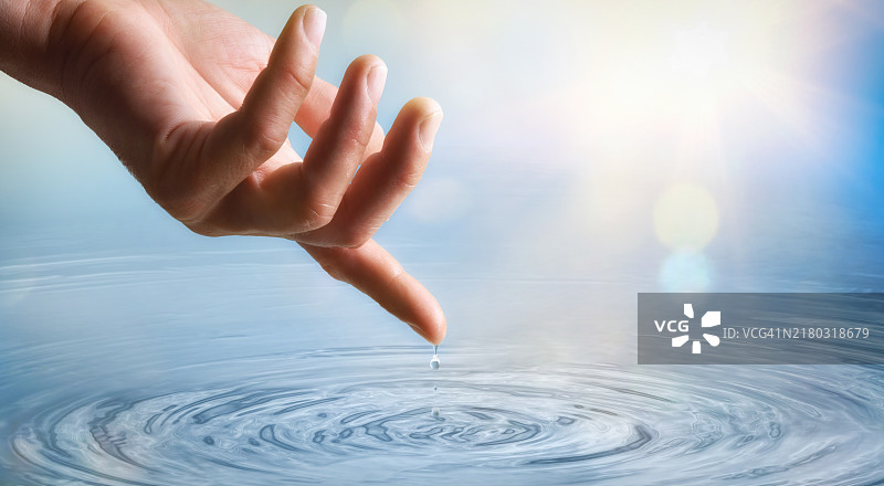 手指上滴落的水珠在水面形成波纹图片素材