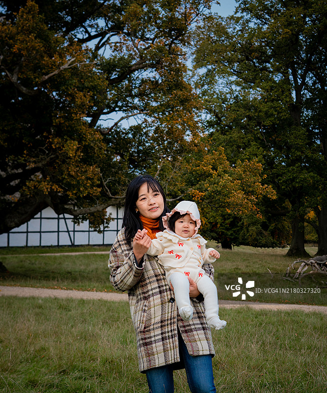 家庭户外时光 - 亚洲女性在森林中享受秋日阳光，怀抱着婴儿图片素材