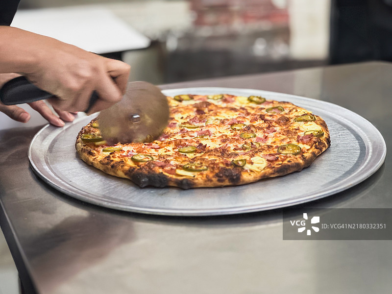 女厨师使用披萨刀切割刚出炉的披萨片图片素材