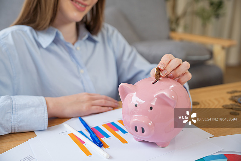 女人的手将硬币放入储蓄罐中以存钱。图片素材