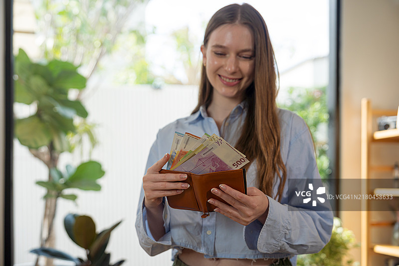年轻女性手持装满欧元钞票的钱包。图片素材