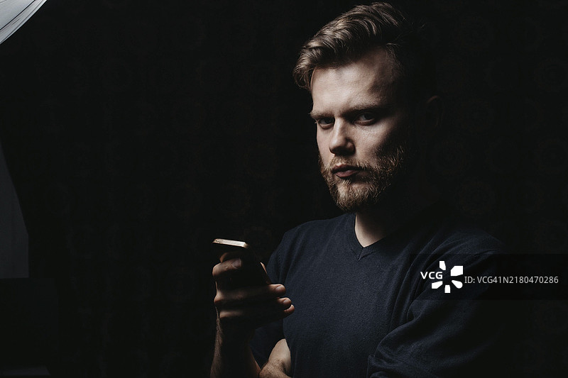 时尚的络腮胡男人手持智能手机，看向镜头图片素材
