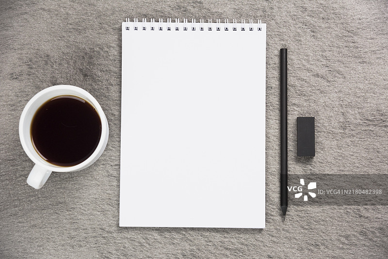 咖啡杯、空白螺旋笔记本、黑色橡皮铅笔灰色桌子的高视角图片素材
