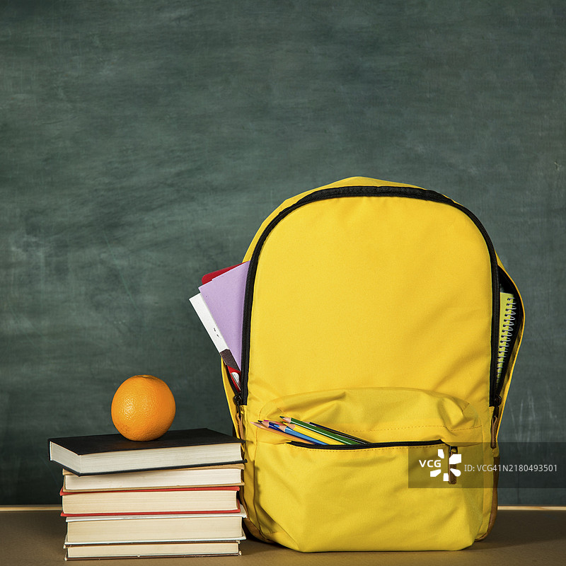黄色背包和堆叠的书本橙色背景图片素材