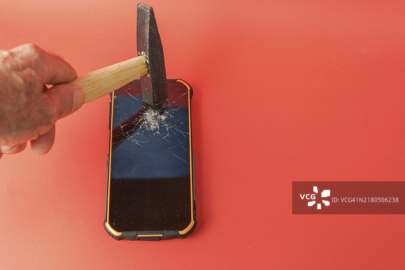 男人用锤子砸碎红色背景上的手机屏幕图片素材
