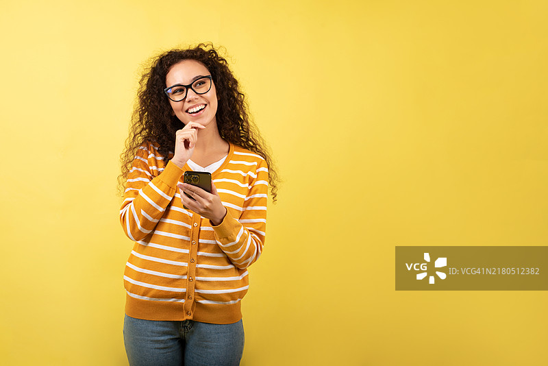 黄色背景下使用手机的深色皮肤女人，视频通讯自拍，录音播客，博主，远程在线工作，智能手机上的对话图片素材