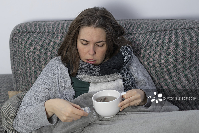 生病的女人盖着毯子在沙发上喝药图片素材
