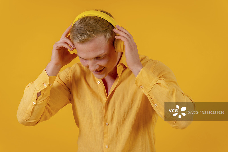 在黄色背景下，戴着无线耳机听音乐和跳舞的白人金发女性。图片素材