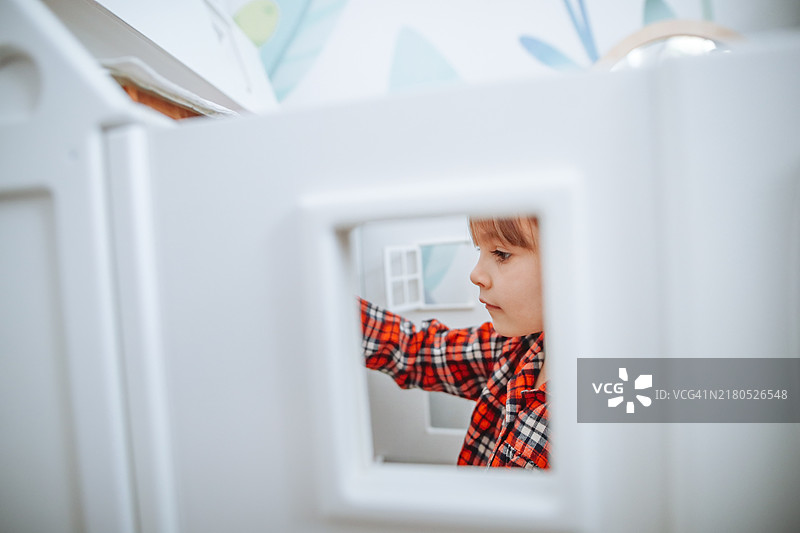 穿着格子睡衣玩大型白色娃娃屋的小孩。窗户视角图片素材