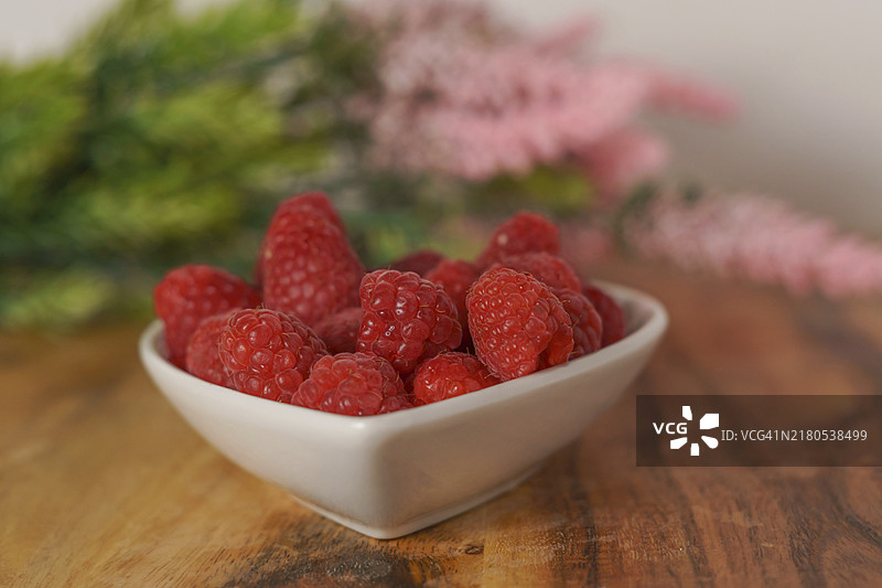 木桌上白色陶瓷碗里的覆盆子图片素材