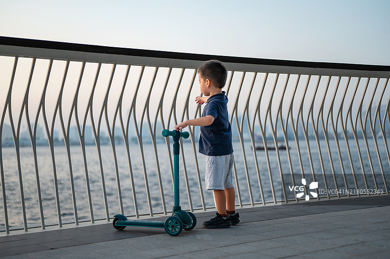 快乐的孩子在海滨栏杆附近拿着滑板车图片素材