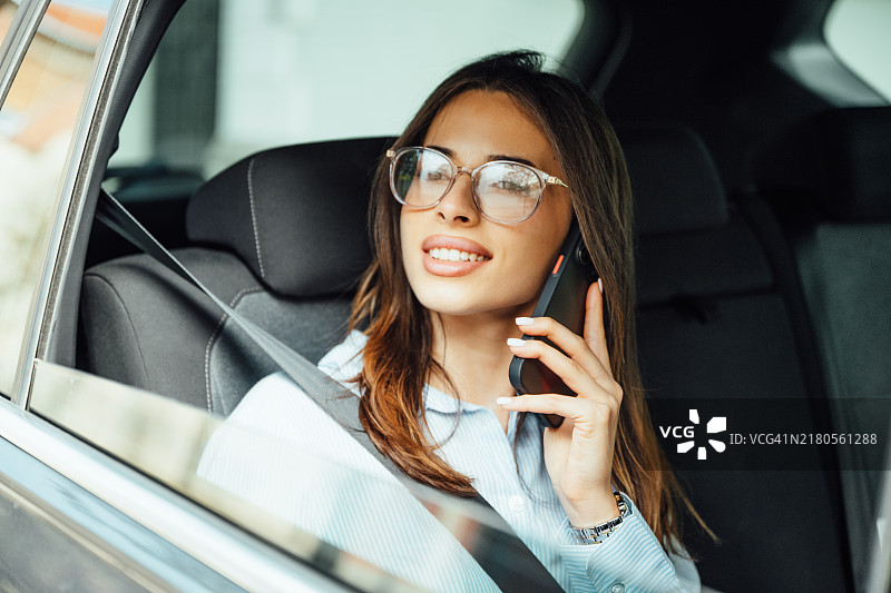 女商人乘坐豪华轿车参加商务会议，在后座上使用智能手机图片素材