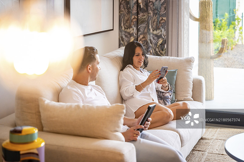 情侣坐在沙发上，在新豪华客厅里使用平板电脑和手机图片素材