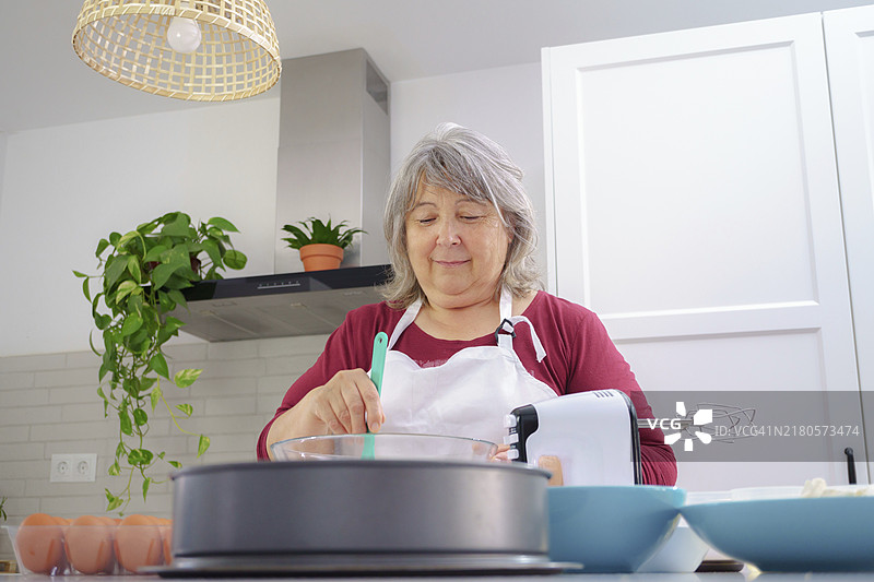 在白色围裙的女厨师用刮刀在碗里打鸡蛋图片素材