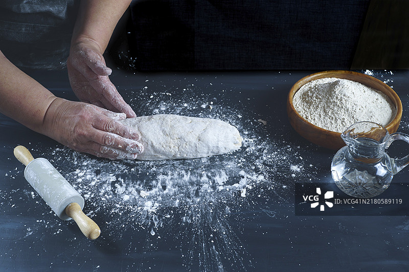 女人用手揉面团，在黑色的木桌上制作自制面包，配有面粉、水和擀面杖图片素材