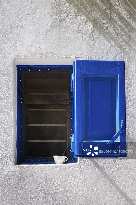 传统希腊岛屿房屋细节。粉刷过的墙壁，带纱窗的小窗户，打开的蓝色防风百叶窗，窗台上的小浓缩咖啡杯，清晨的阳光，柔和的阴影。地中海生活方式，甜蜜生活，日常仪式，假期图片素材