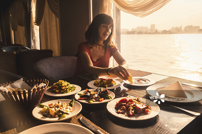 在尼罗河的船上享用晚餐的年轻游客，这是一顿传统的埃及餐，窗户里有日落的光芒。非洲图片素材