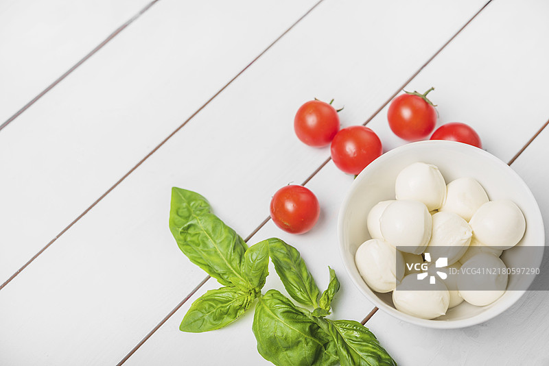 马苏里拉奶酪球配罗勒叶红番茄木纹白色背景图片素材