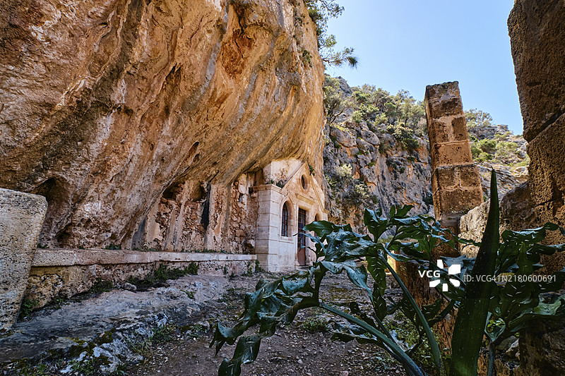 位于希腊克里特岛哈尼亚阿克罗蒂里半岛阿夫拉基峡谷废弃的卡托利科修道院中圣约翰隐士的正统洞穴教堂。 入口和路径的春季日间照片。 选择性聚焦图片素材