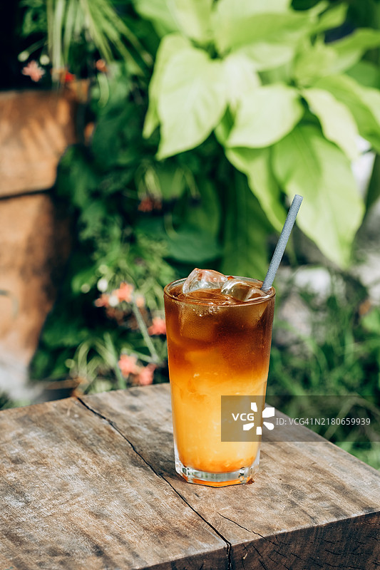 清爽的冰咖啡饮料，搭配新鲜橙汁，盛在高脚杯中，背景是郁郁葱葱的绿叶。图片素材