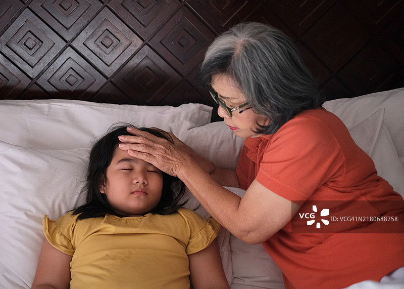 印尼祖母在床上查看生病孙女的体温图片素材