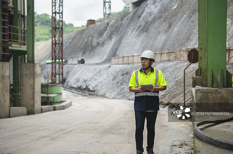 专业的亚洲男性工业工程师在制造工厂内站着使用平板电脑。正在制造厂或生产厂工作。图片素材