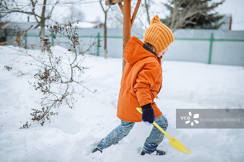 穿着针织帽子和夹克在雪地后院行走的孩子图片素材