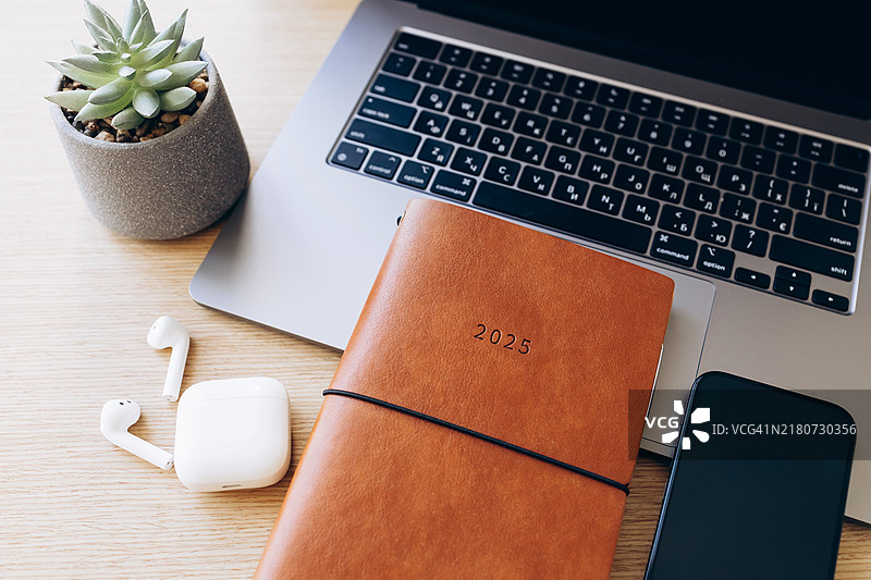 现代工作空间平铺，包含2025年计划本、笔记本电脑、智能手机和木质桌面上的多肉植物。简约的办公环境，旨在提高生产力和规划。图片素材