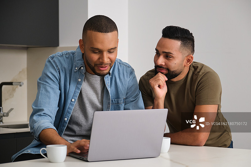 两个男人在厨房里用笔记本电脑，对着屏幕上的东西微笑图片素材