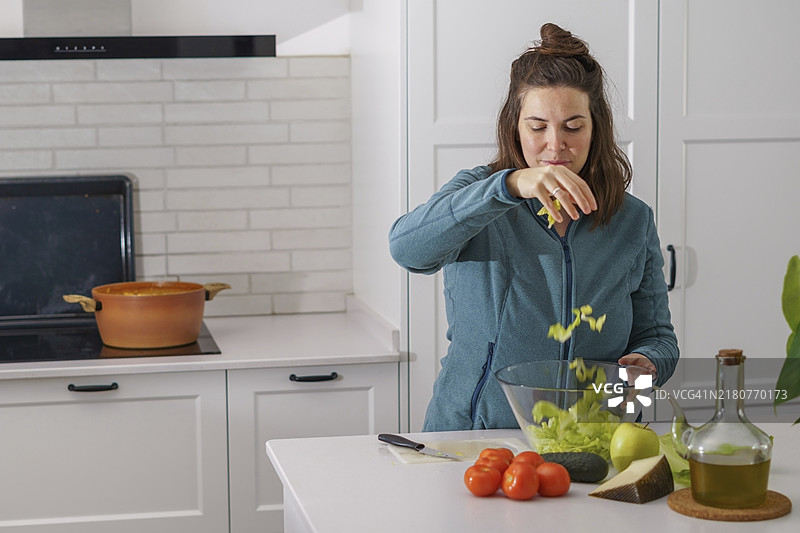 年轻深色头发女孩在厨房切生菜准备沙拉图片素材