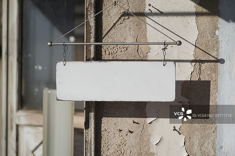 一块白色矩形招牌悬挂在金属杆上，背景是有裂纹和剥落油漆的纹理墙壁。图片素材